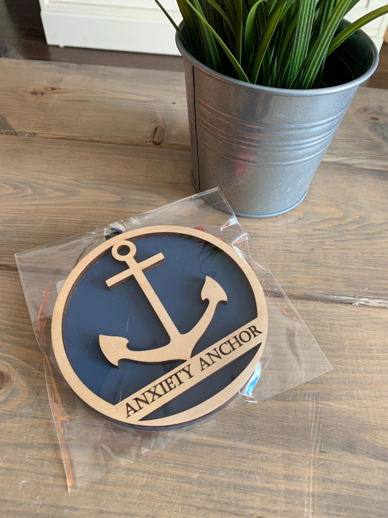 A wooden Anxiety Anchor ornament on a table beside a green plant